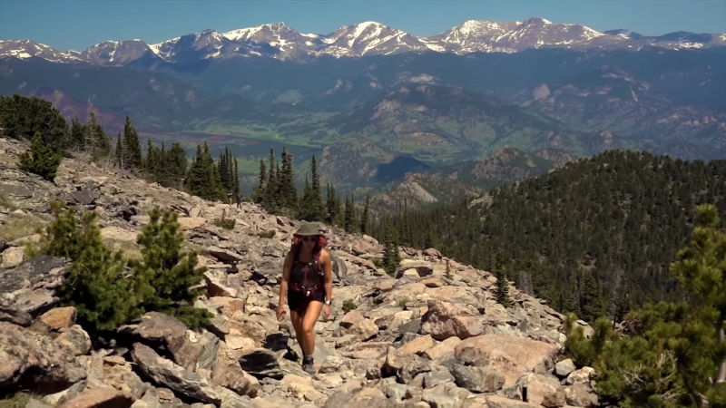 A hiker on a rocky trail with mountain peaks in the background at Rocky Mountain National Park